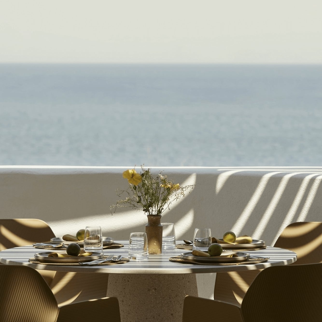 Pārocks, Europe — Seaside dining table with striped linen chairs, yellow flowers, geometric shadows, minimalist coastal architecture with ocean horizon view.