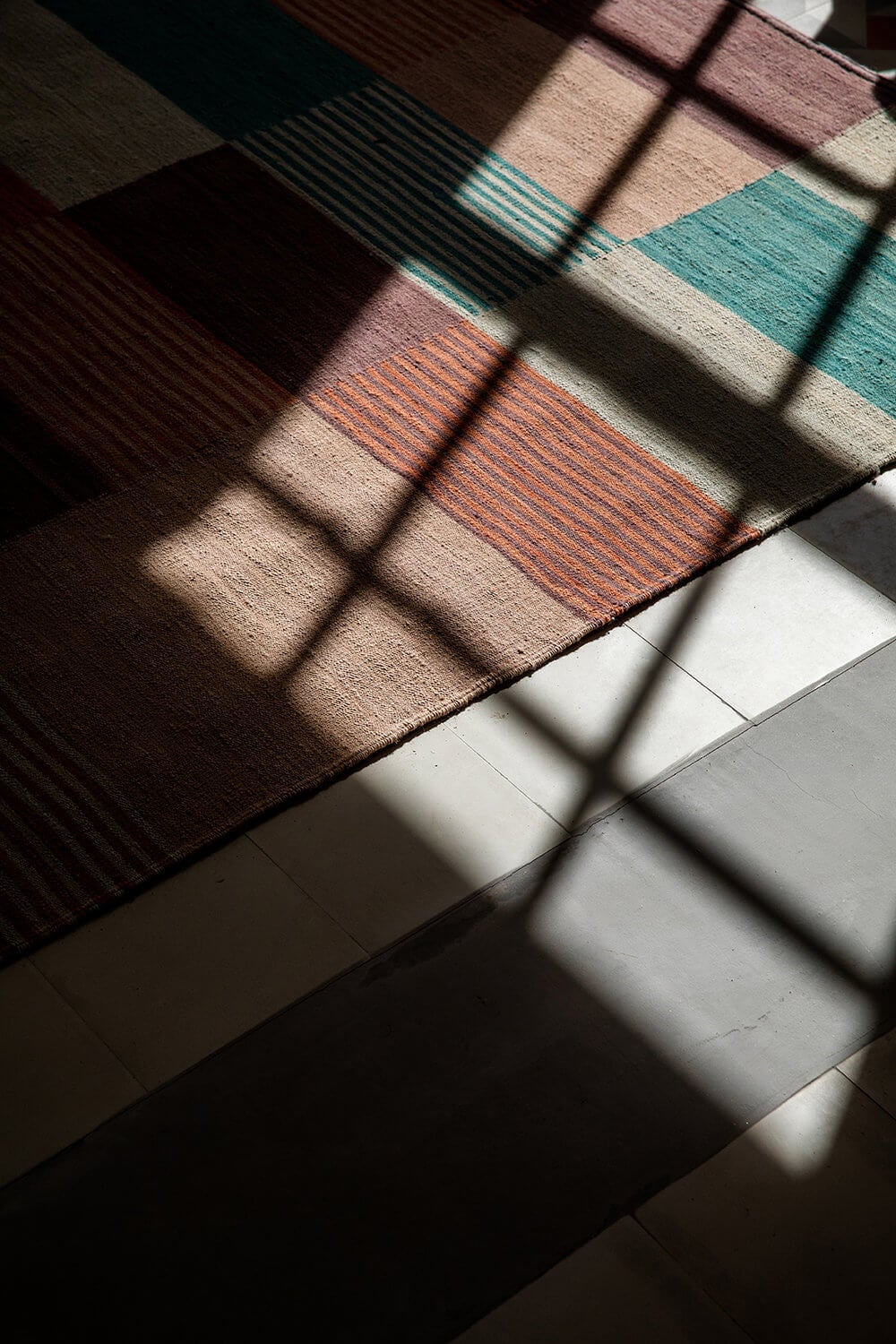Es Bec d’Aguila — Es Bec d'Aguila, Balearic Islands, Spain — Striped textiles and window shadows cast geometric patterns across terracotta and cream floor tiles in warm afternoon light.
