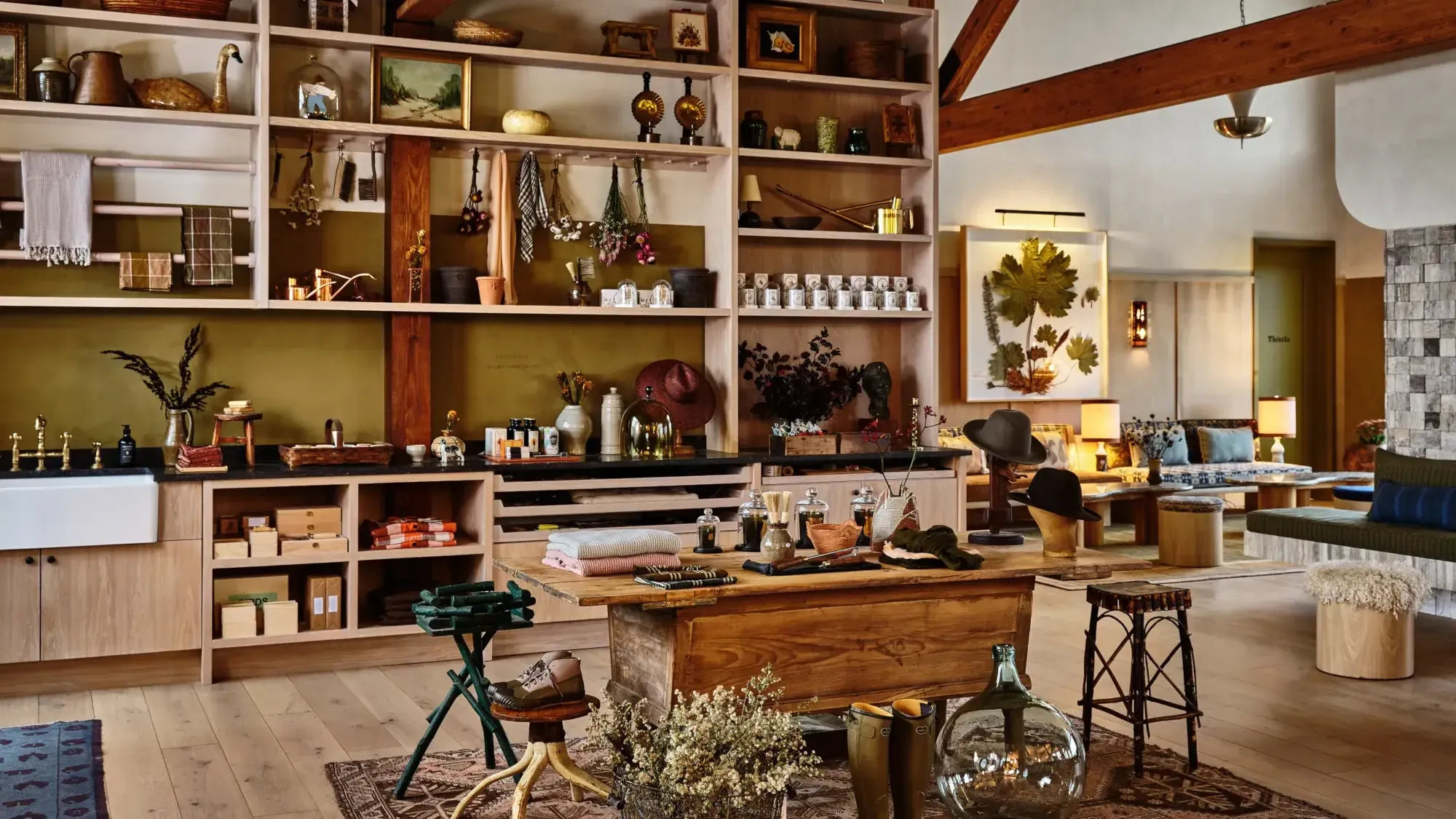 The Shop by Gardenheir, North America — Retail interior with olive-backed shelving, wooden counter, exposed beams, brass fixtures, and curated home goods displaying botanical and artisanal products.