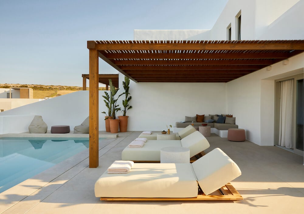 Pārocks, Europe — Modern poolside terrace with cream loungers, wooden pergola, white architecture, and minimalist garden in golden light.