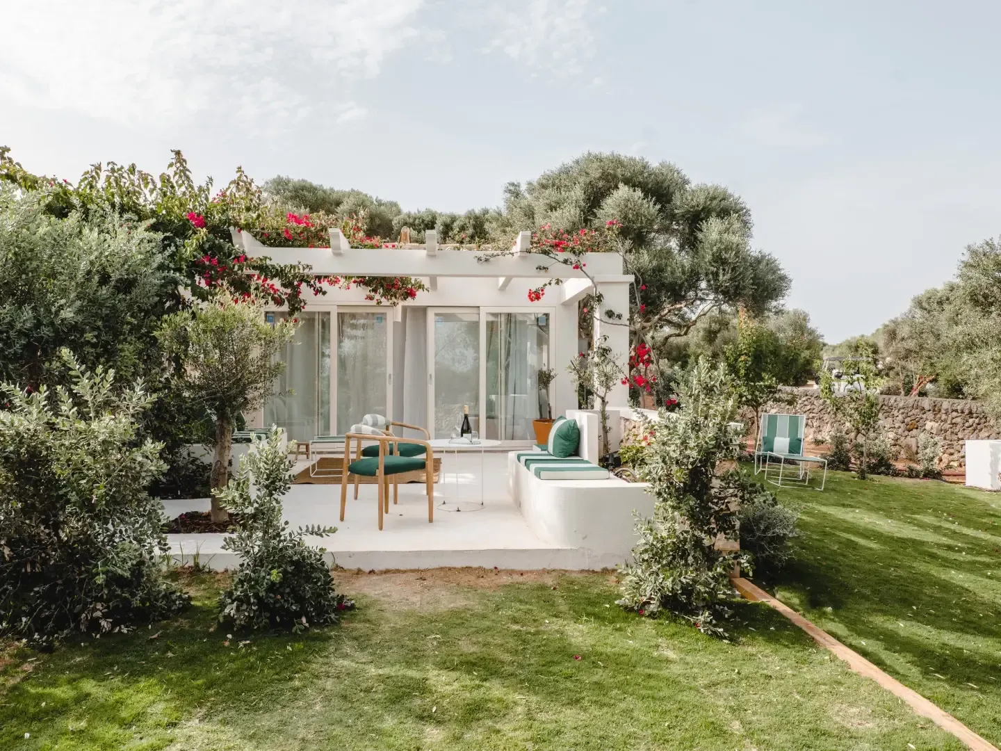 Morvedra Nou, Balearic Islands — Minimalist white guest pavilion with bougainvillea, olive trees, and furnished terrace overlooking Mediterranean landscape.