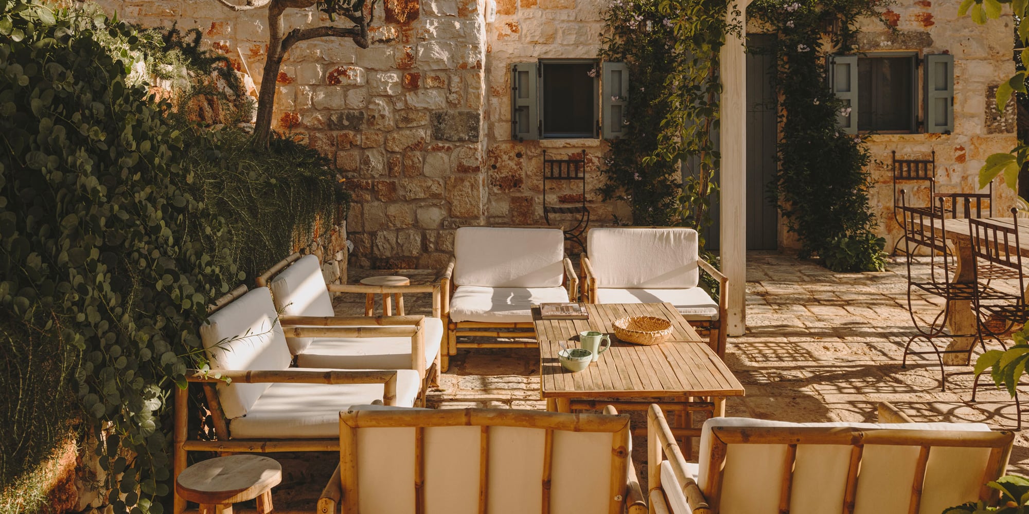 Masseria Moroseta, Europe — Courtyard with weathered stone walls, wooden loungers with cream cushions, ivy-covered facades, and dappled sunlight casting shadows across terracotta flooring.
