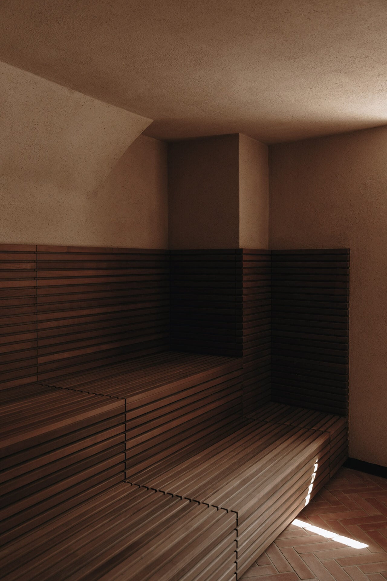 Parkhotel Mondschein, Europe — Minimalist sauna interior with tiered wooden benches, warm plaster walls, and geometric light casting through architectural apertures.