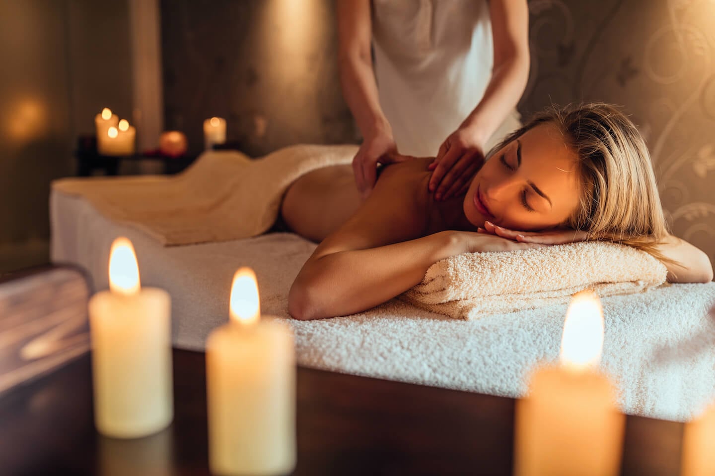 Pārocks Spa, Europe — Woman receiving back massage on padded table surrounded by lit candles, warm ambient lighting, neutral linens and spa ambiance.