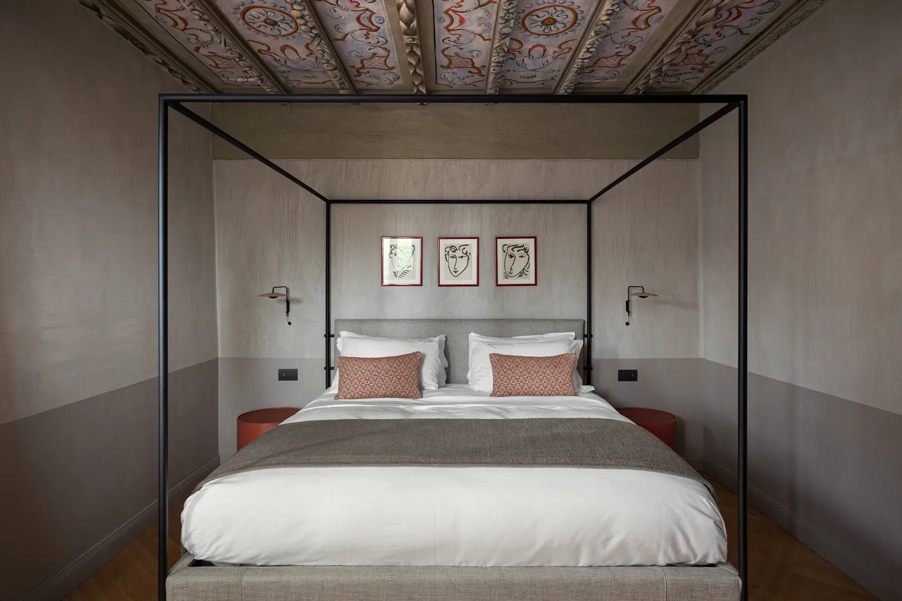 Roncolo 1888, Europe — Modern canopy bed with black frame, white linens, coral pillows beneath ornate painted ceiling, minimalist wall art, neutral palette.
