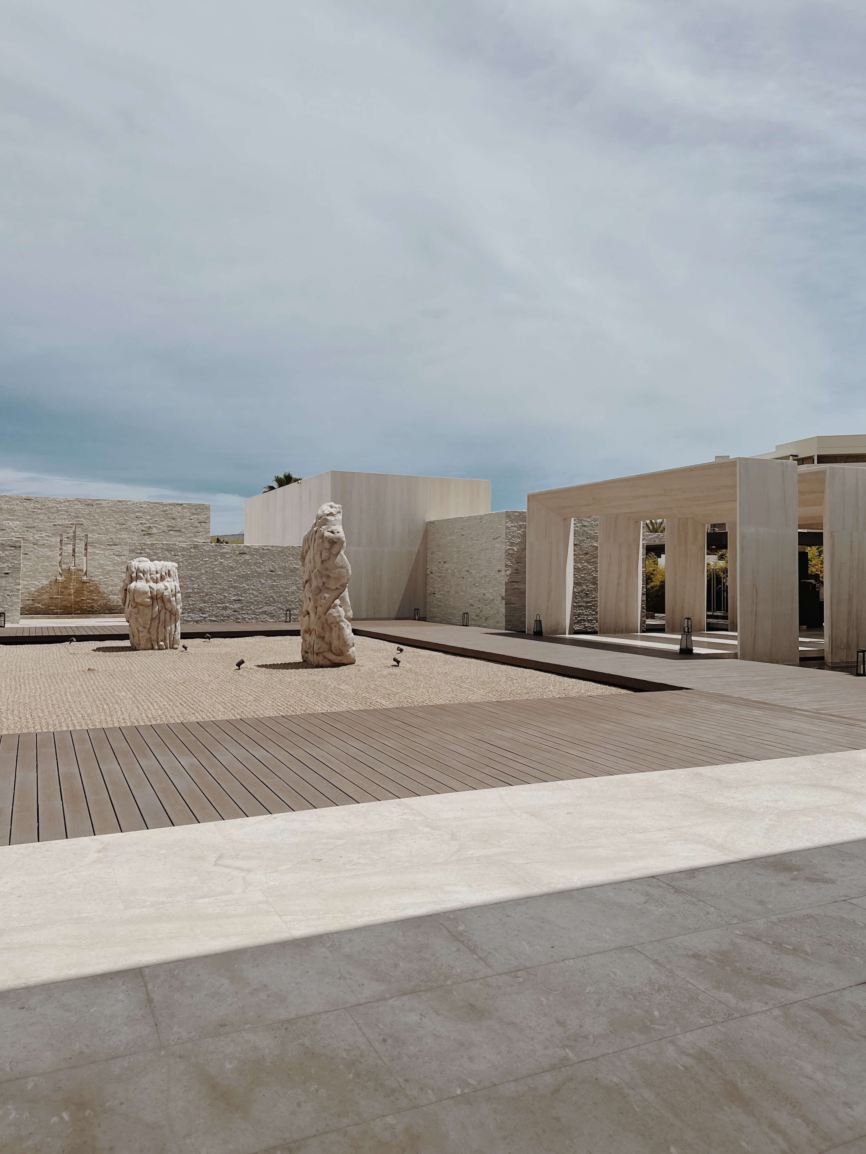 Nobu Los Cabos, Mexico — Minimalist courtyard with stone sculptures, wooden deck, geometric architecture, and natural light casting sharp shadows.