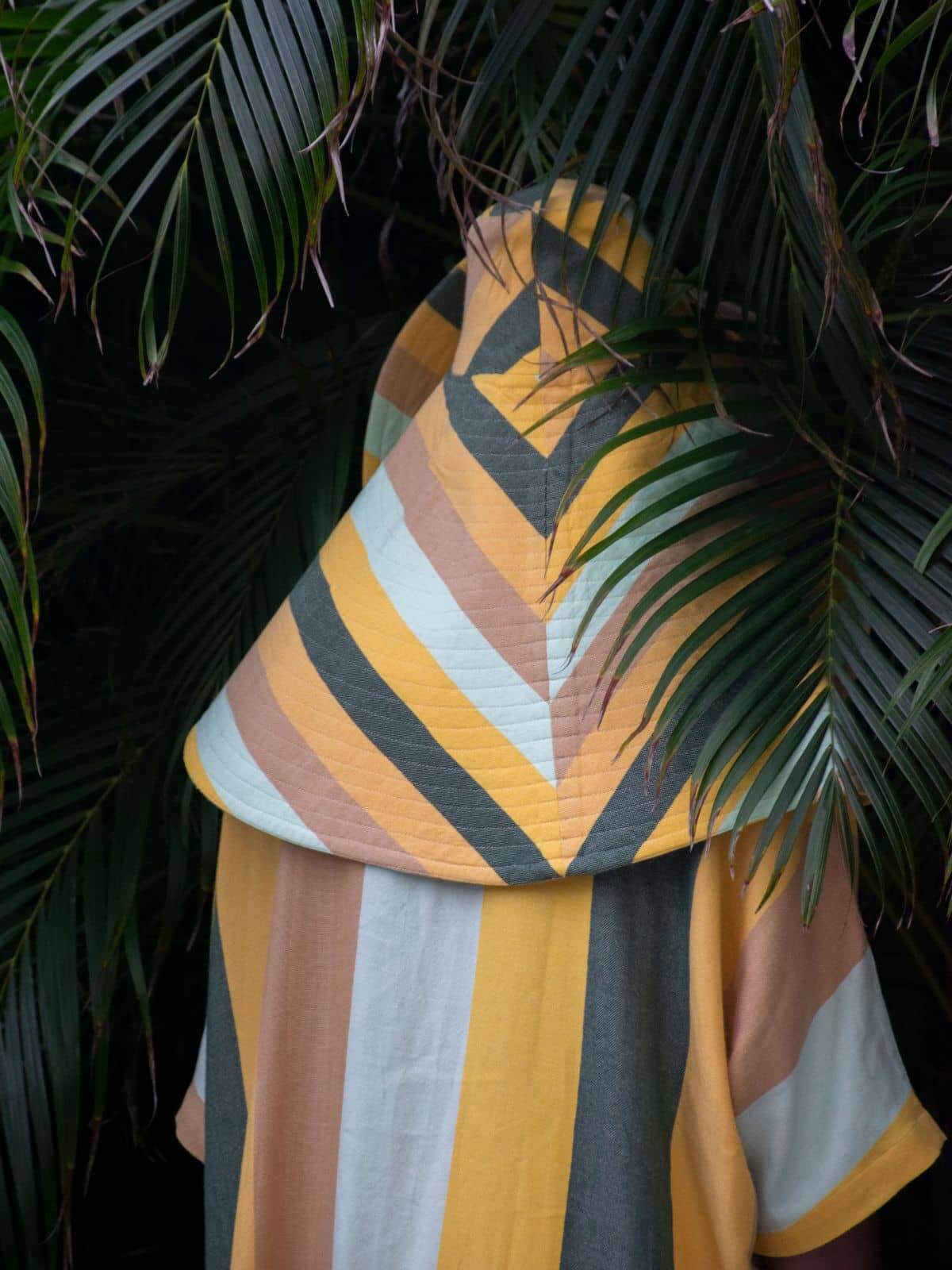 Palm Heights Store, North America — Striped linen throw in yellow, charcoal, cream and taupe draped over palm fronds, tropical resort textile detail.