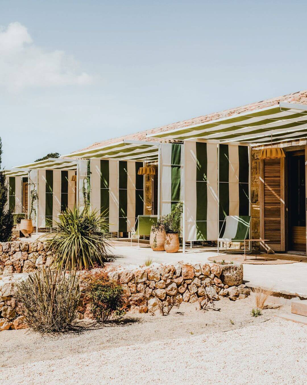 Amagatay, Balearic Islands — Modernist pavilions with striped awnings, stone walls, and terracotta pottery beneath clear Mediterranean sky.