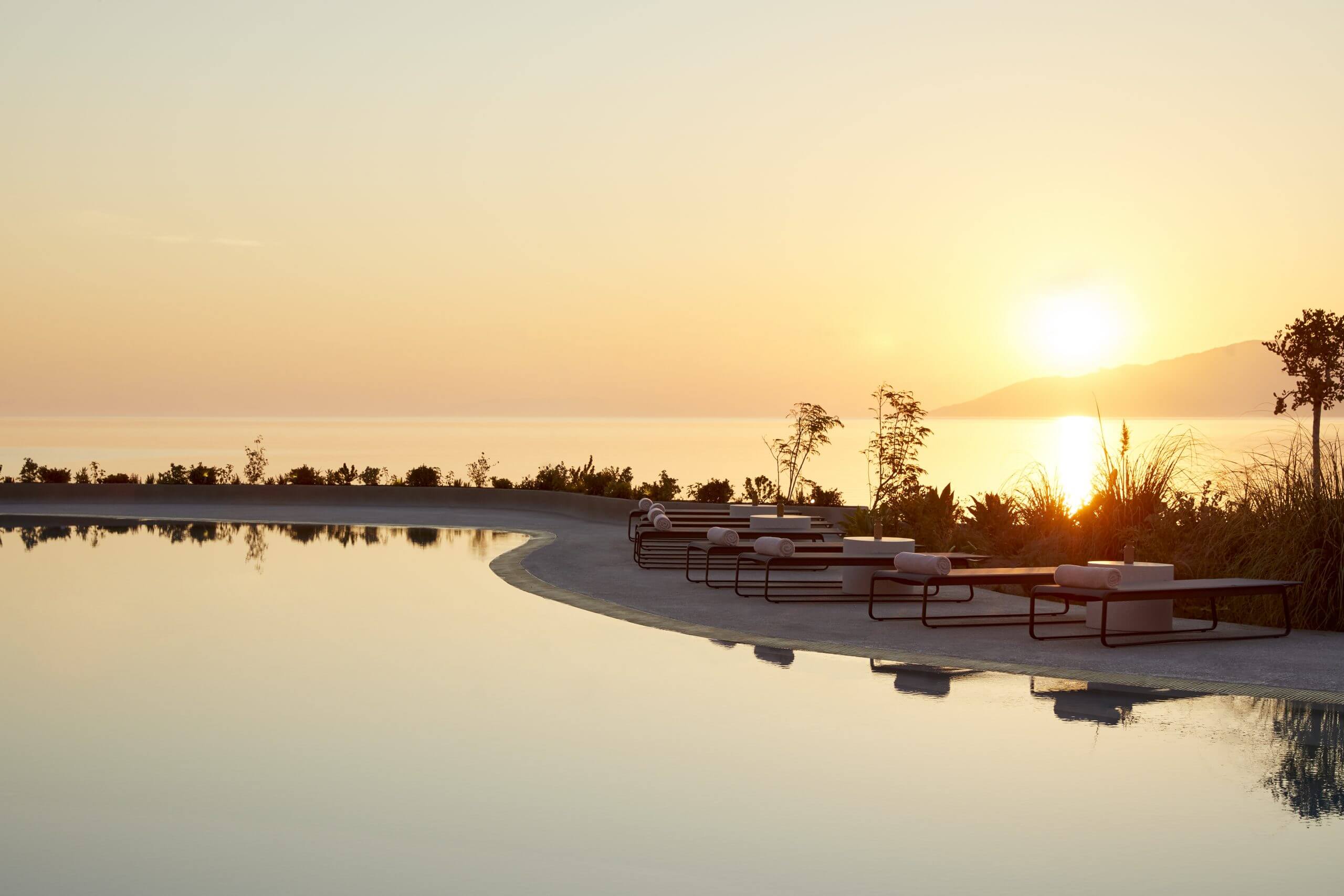 Pārocks, Europe — Curved concrete platform with metal bench seating overlooking still water at sunset, minimalist hospitality design.