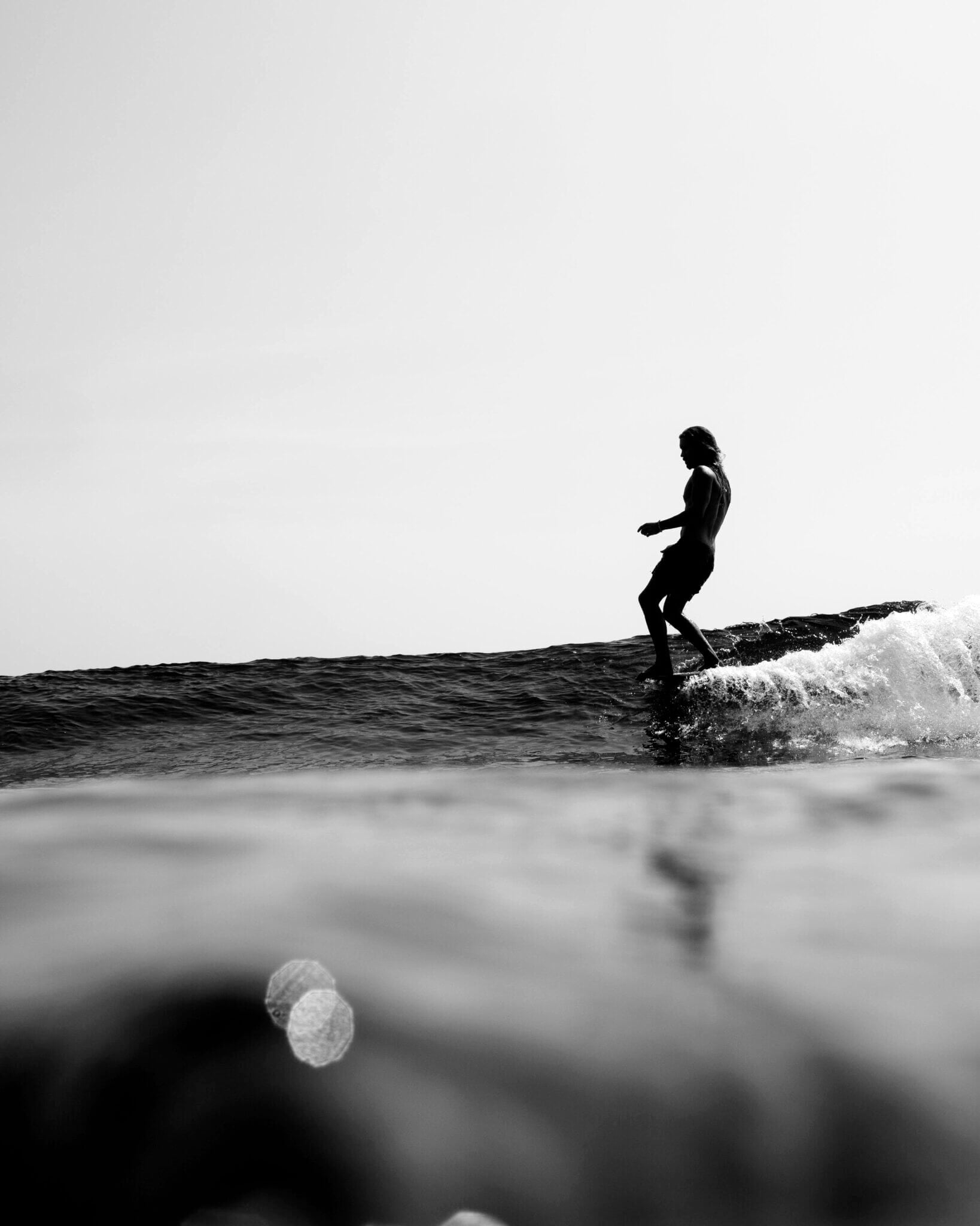 Further Hotel, Asia — Silhouetted surfer riding wave at dusk, black and white coastal photography capturing dynamic ocean movement and minimalist seascape.