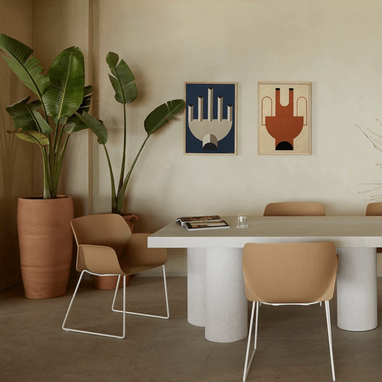 Pārocks, Europe — Minimalist dining space with terrazzo table, tan chairs, potted banana plants, and geometric wall art in navy and rust tones.
