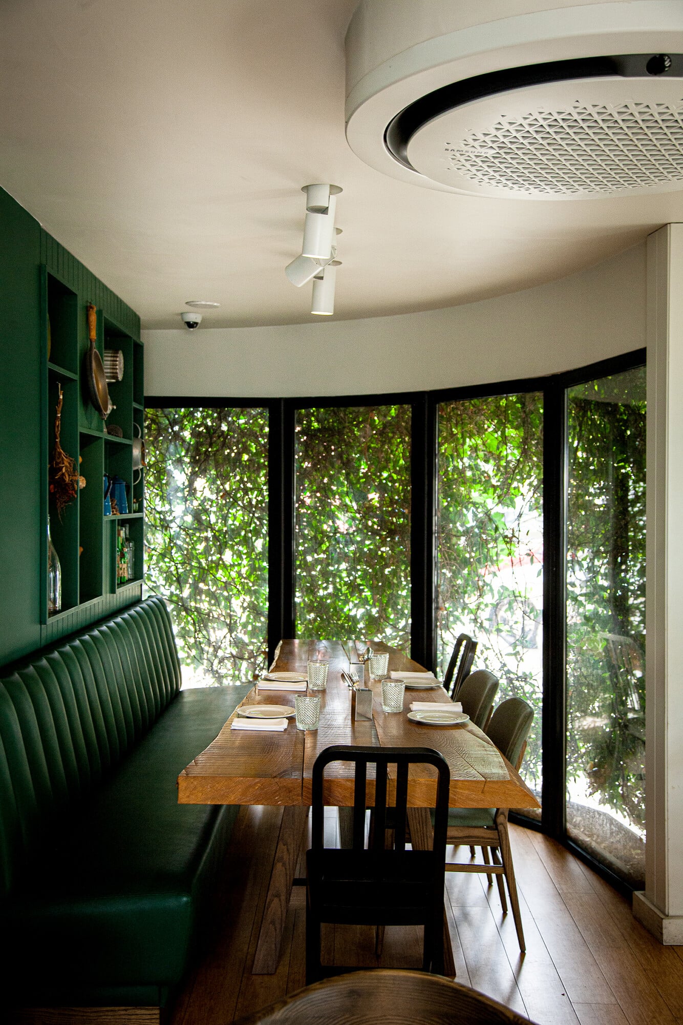 Tasca da Esquina, Portugal — Curved banquette dining room with verdant garden views through floor-to-ceiling windows, wooden table, black chairs, cream ceiling with sculptural light fixture.