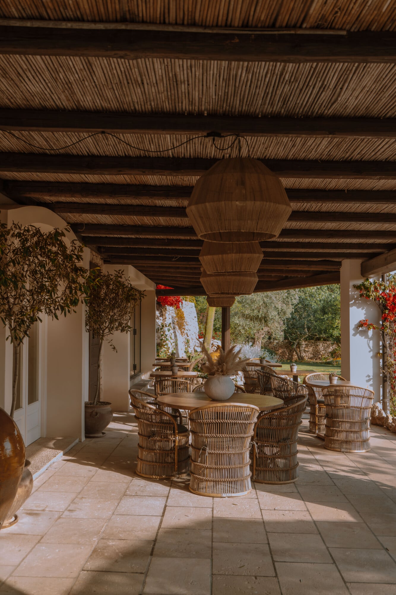 Tenuta Negroamaro, Europe — Covered terrace with woven pendant light, rattan chairs, stone flooring, and garden views through open colonnade.