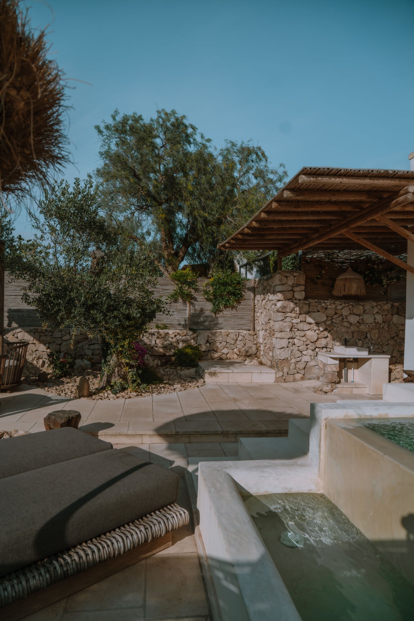 Stone courtyard at Tenuta Negroamaro with wooden pergola, loungers, and shallow reflecting pools under clear sky.