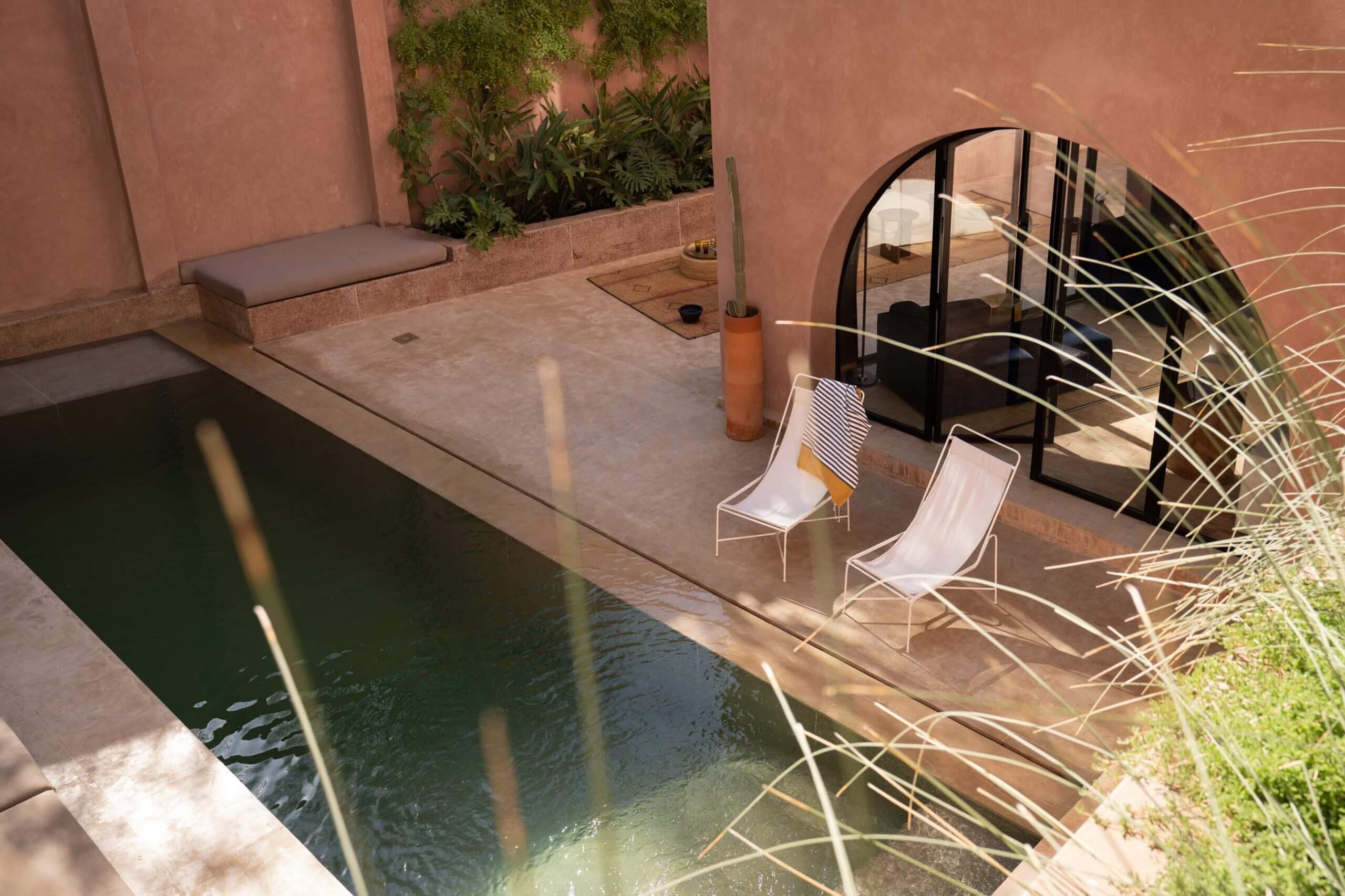Maison Brummell Majorelle, Africa — Ochre courtyard with rectangular pool, loungers, and arched glass door overlooking minimalist interior spaces.