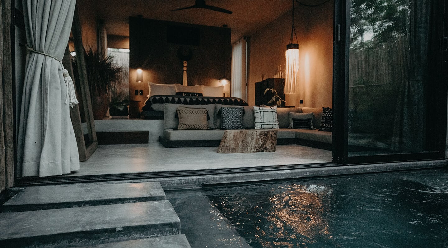 Bardo, Mexico — Candlelit poolside lounge with curved seating, geometric pillows, and glass doors opening to terrace at dusk.