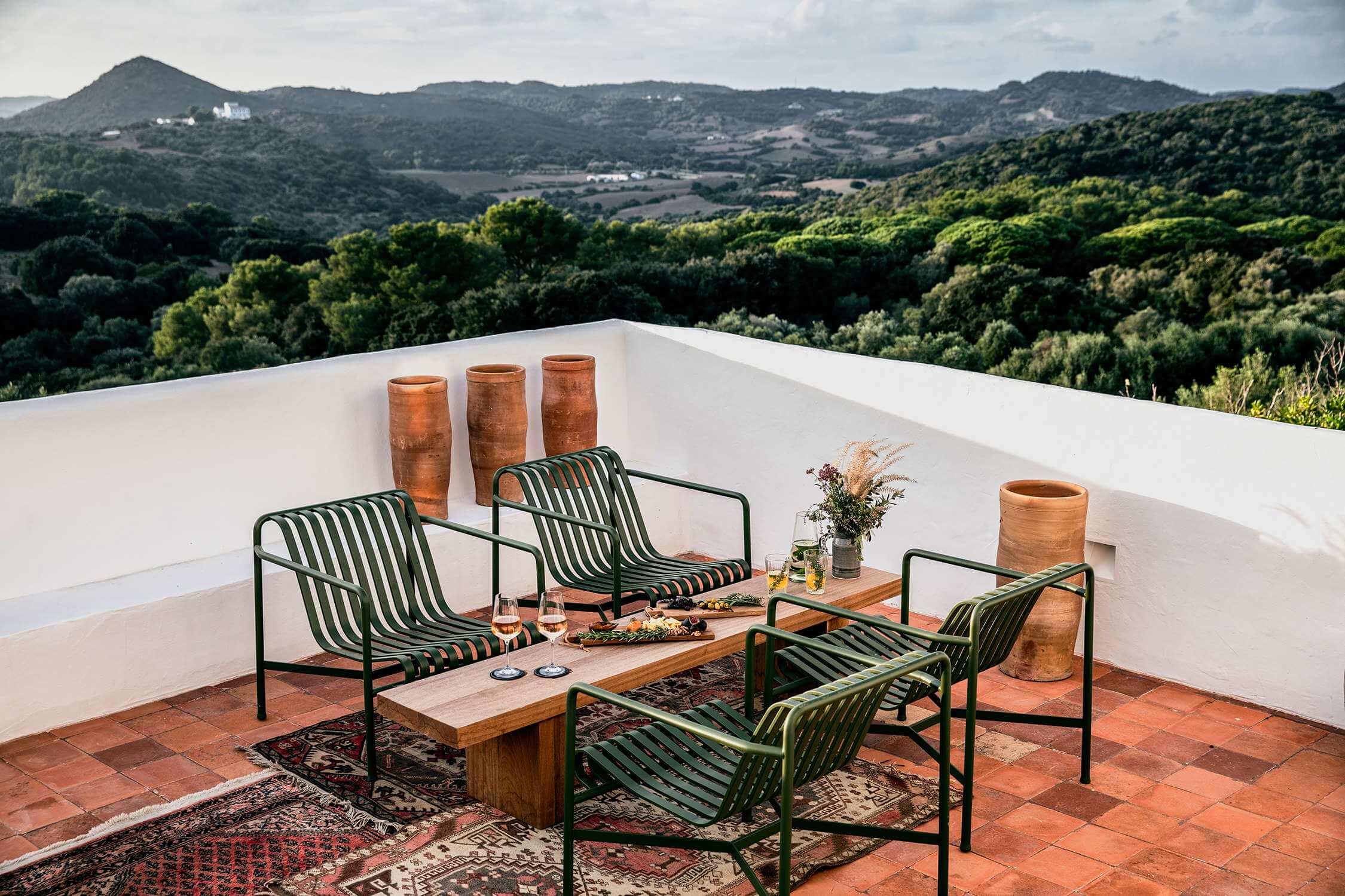 Es Bec d’Aguila — Es Bec d'Aguila, Balearic Islands — Rooftop terrace with striped green lounge chairs, wooden table, terracotta vessels, overlooking forested valleys and distant hills.