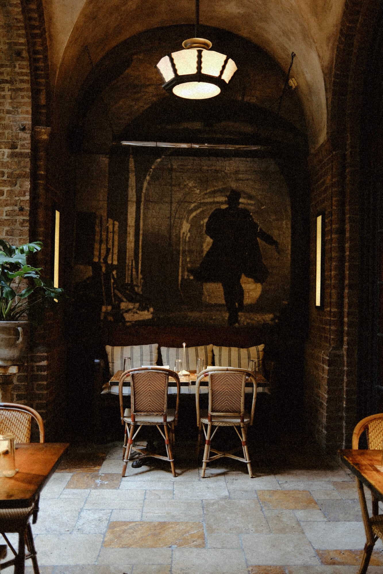 The Greenwich Hotel, New York, United States — Arched brick corridor with rattan chairs, warm pendant lighting, and atmospheric mural in luxury hospitality setting.