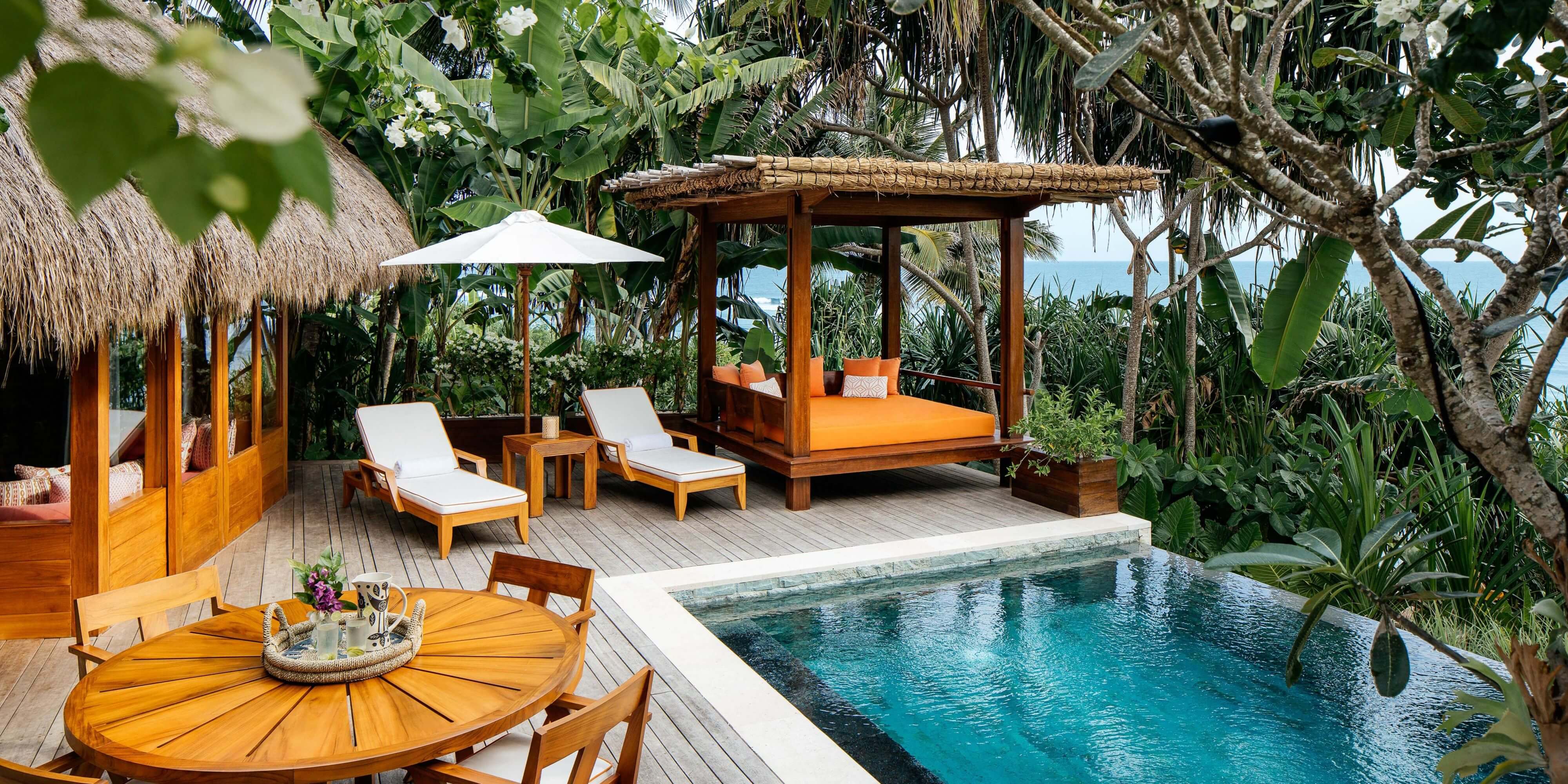 NIHI Sumba, Asia — Teak pavilion with canopy bed and loungers overlooking turquoise pool, tropical garden, ocean view, warm wood tones, refined island resort design.