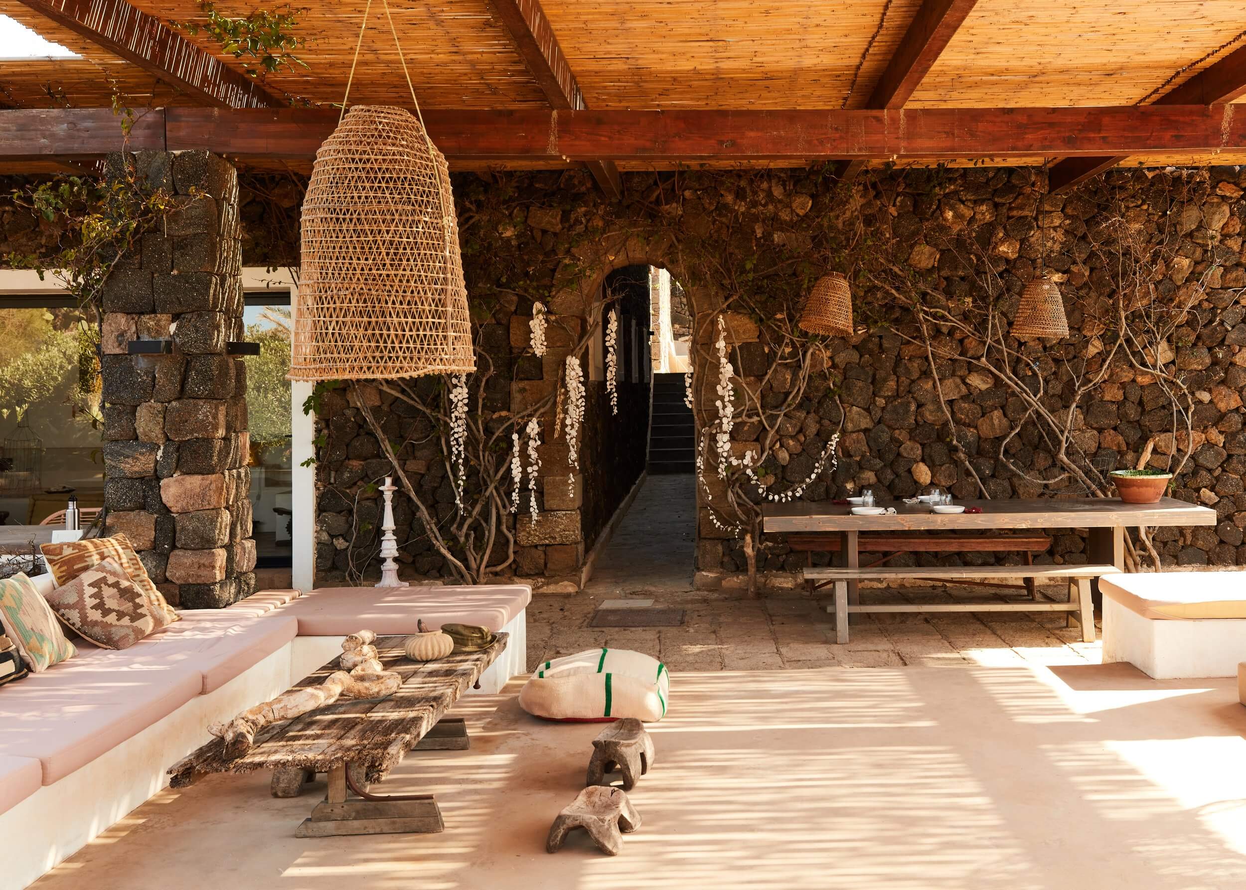 Parco Dei Sesi, Europe — Stone terrace with woven pendant lamp, pink seating, climbing vines, wooden beams, and natural light filtering through covered pavilion.