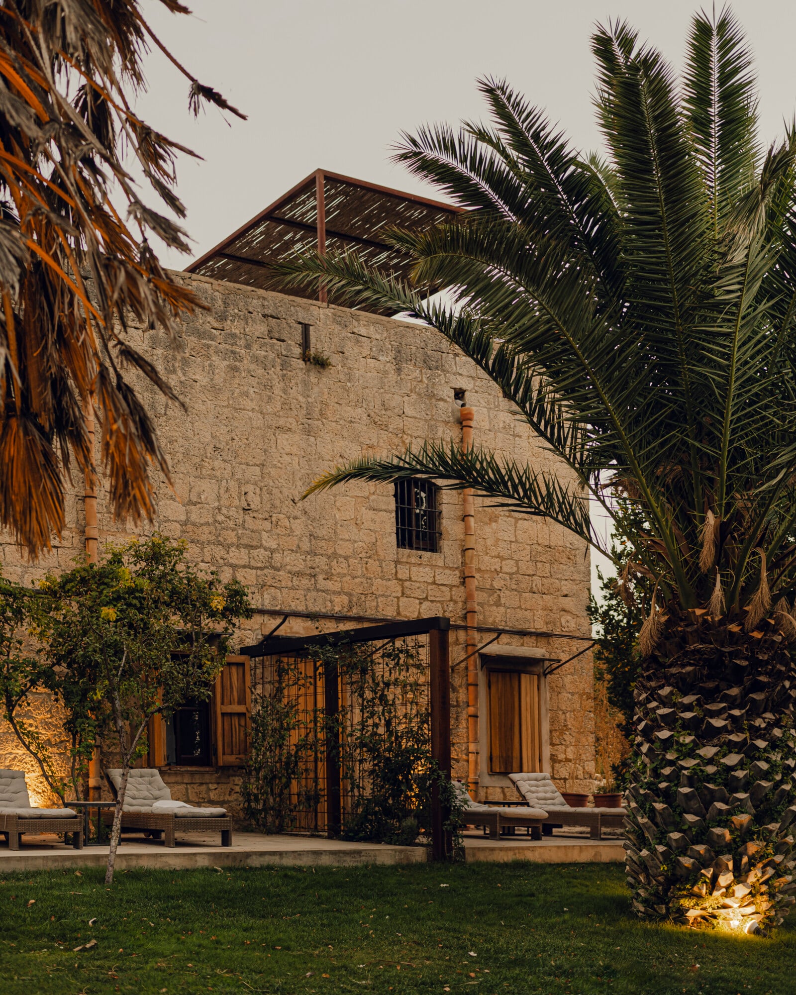 Susafa, Italy — Stone villa with palm trees, wooden pergola, loungers on lawn, minimalist Mediterranean luxury architecture and landscape design.