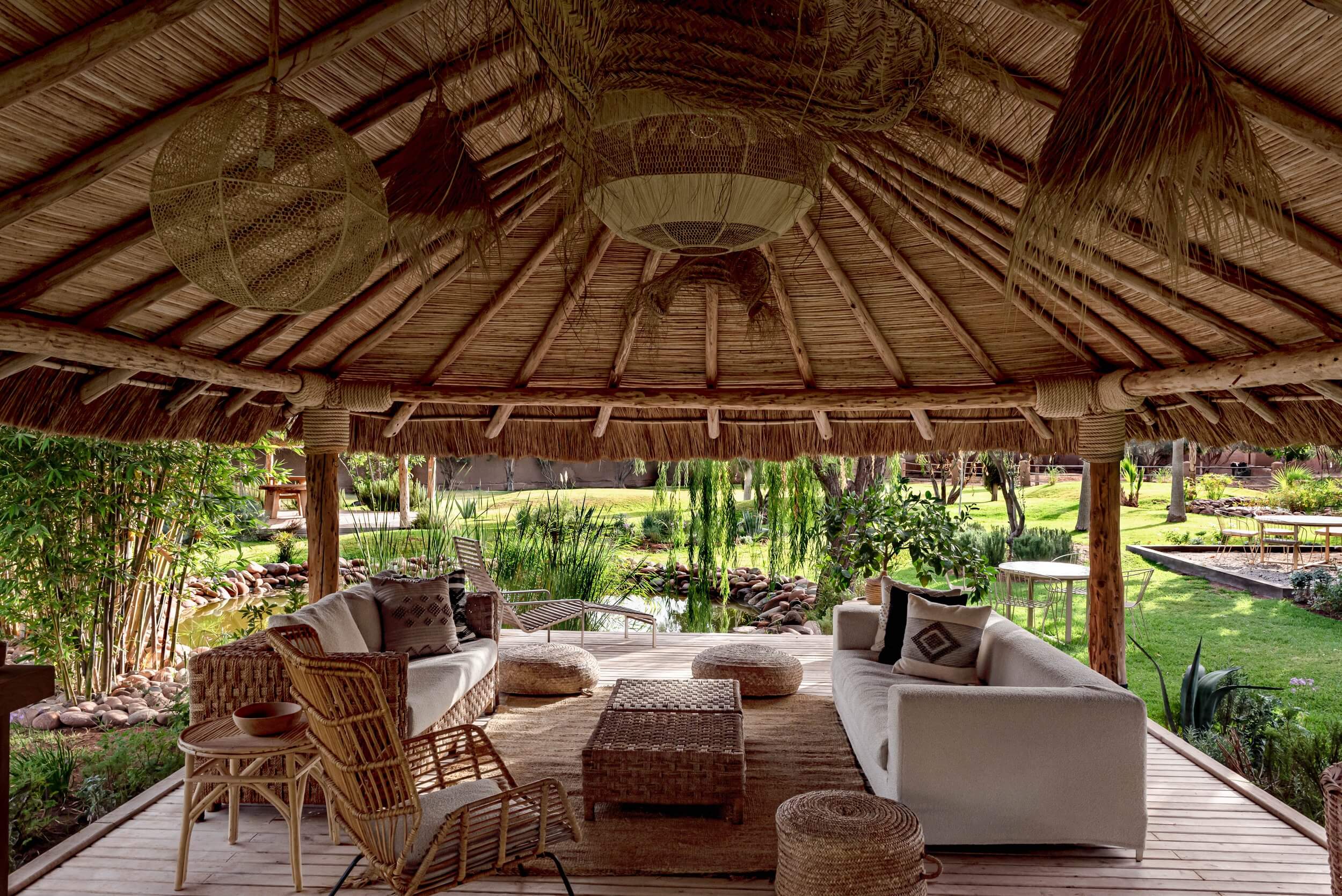 Villa D, Africa — Thatched pavilion with woven ceiling, cream linen seating, woven ottomans, overlooking manicured gardens and water features.