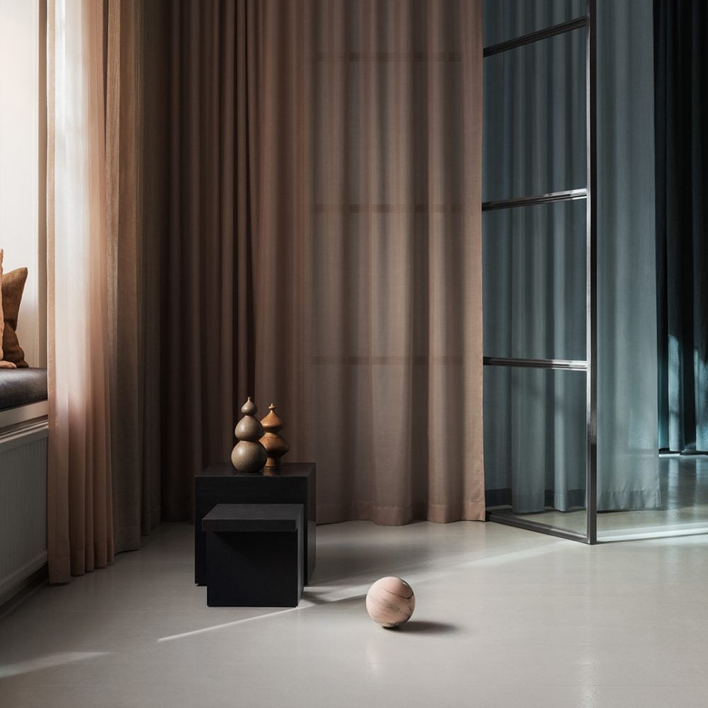 Astrid’s Textile Lab — Astrid's Textile Lab, Europe — Minimalist interior with floor-to-ceiling taupe curtains, black cubic furniture, wooden spheres, polished concrete floors, and modern glass partition.