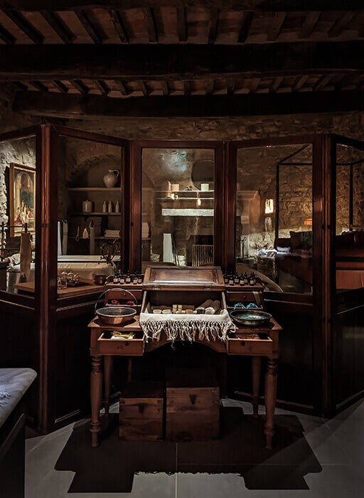 Castello di Reschio, Europe — Wooden display cabinet with glass doors showcasing artisan jewelry and accessories, warm ambient lighting, rustic stone walls, heritage craftsmanship.