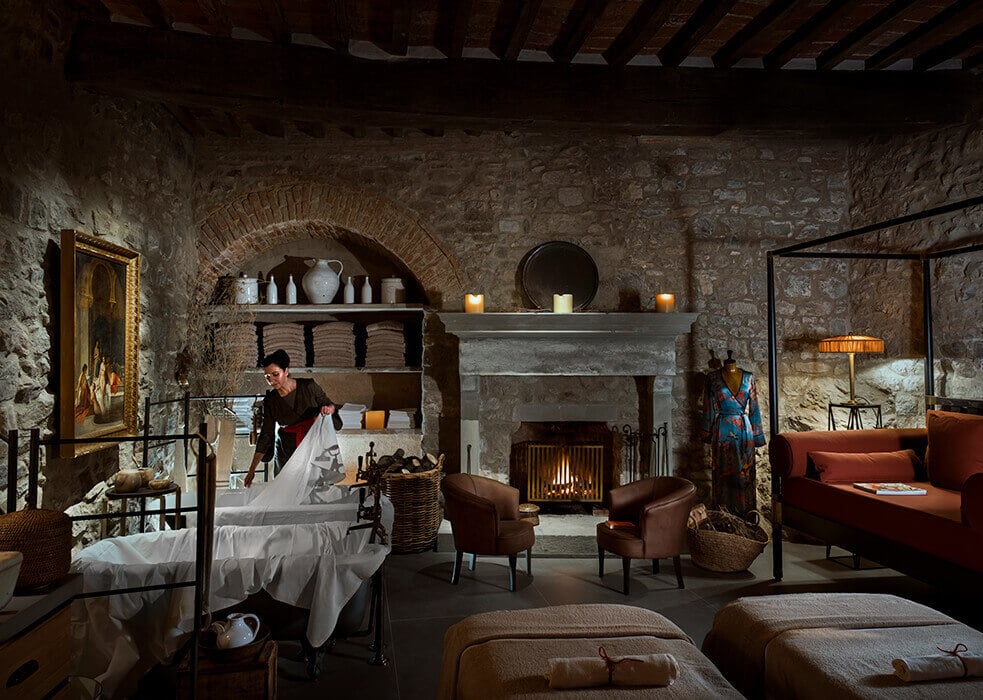 Castello di Reschio, Umbria, Italy — Stone medieval bedroom with arched fireplace, exposed beams, terracotta furnishings, and candlelit ambiance.