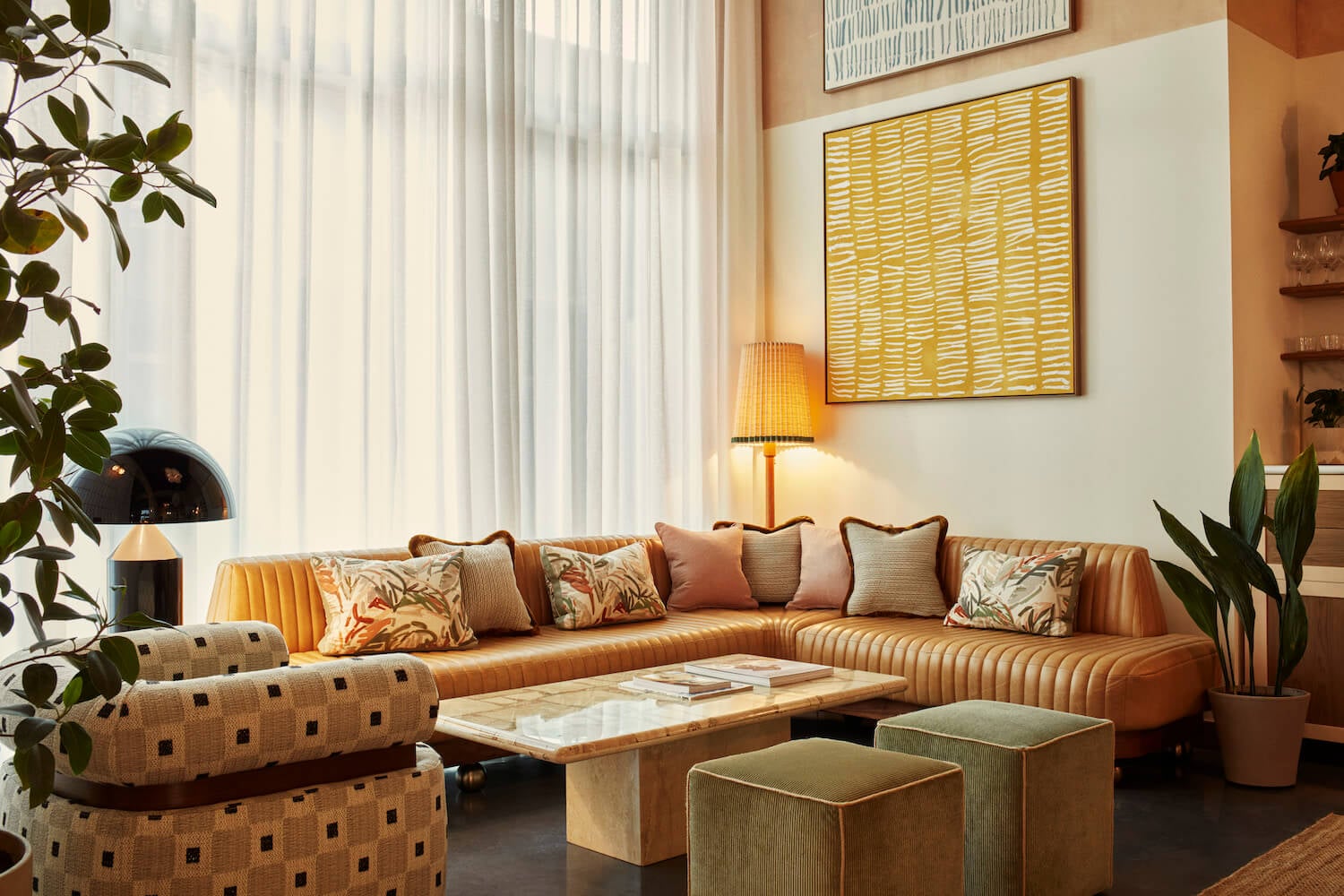 The Hoxton Poblenou, Barcelona, Spain — Sectional sofa with patterned armchair, natural wood coffee table, woven ottomans, warm lighting, and botanical accents in contemporary living room.