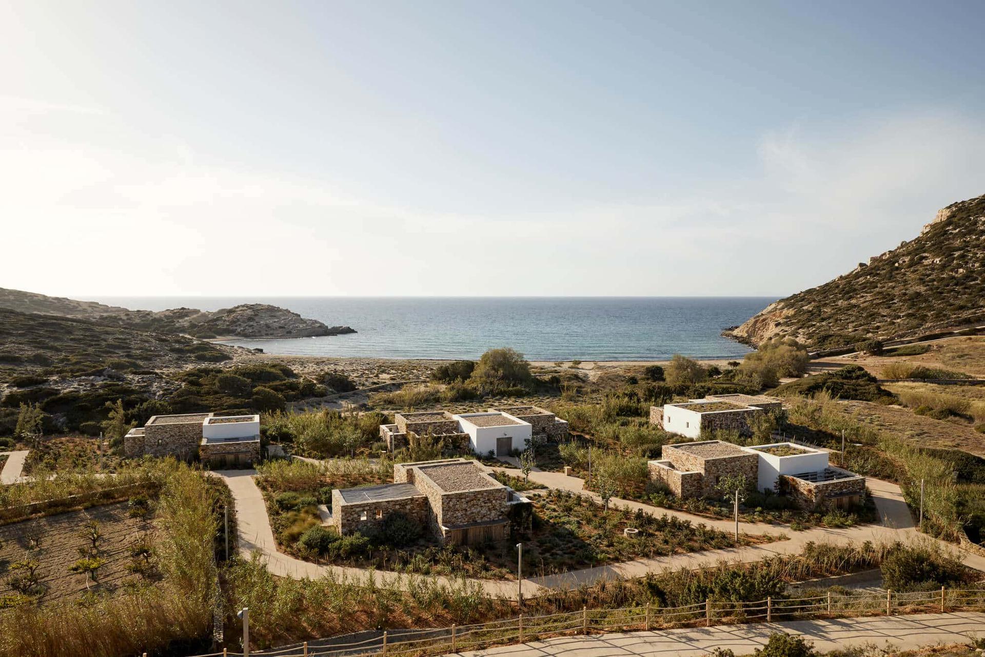The Rooster, Europe — Coastal stone villas with white-rendered walls nestled on Mediterranean hillside overlooking turquoise bay, minimalist architecture, natural landscape integration.