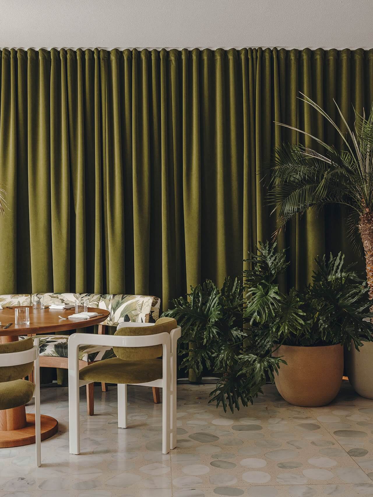 Jara, Balearic Islands — Olive linen curtains frame a dining space with mid-century chairs, terracotta planters, and terrazzo flooring in natural light.