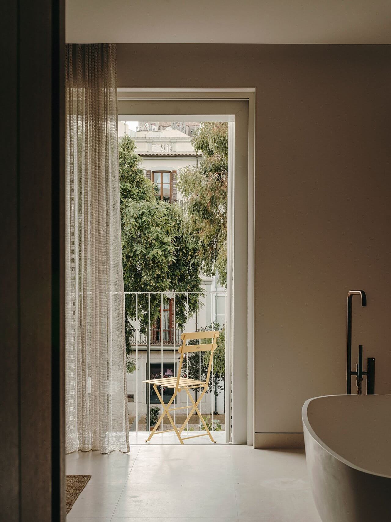 The Standard Ibiza, Balearic Islands, Spain — Minimalist bathroom with freestanding tub opening to Mediterranean courtyard with climbing vines and wooden chair.
