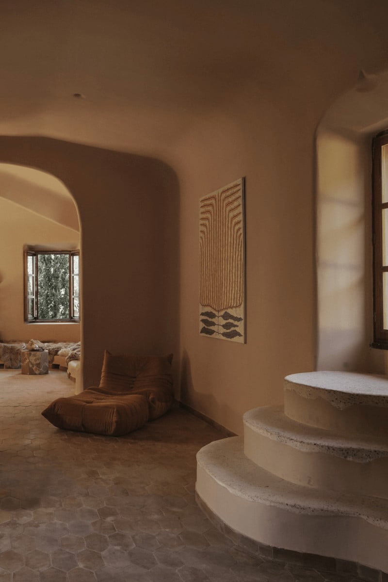Hotel Corazón, Balearic Islands — Terracotta-walled interior with curved archways, concrete spiral staircase, geometric wall art, warm natural light, minimalist luxury design.