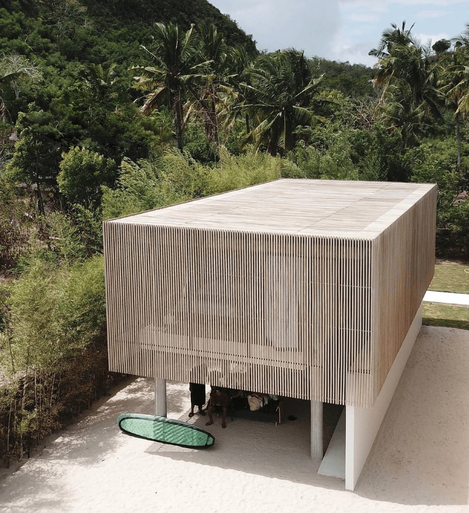 Innit Lombok, Asia — Wooden pavilion with slatted timber screens and concrete base beneath tropical jungle canopy, surfboard leaning against support post.