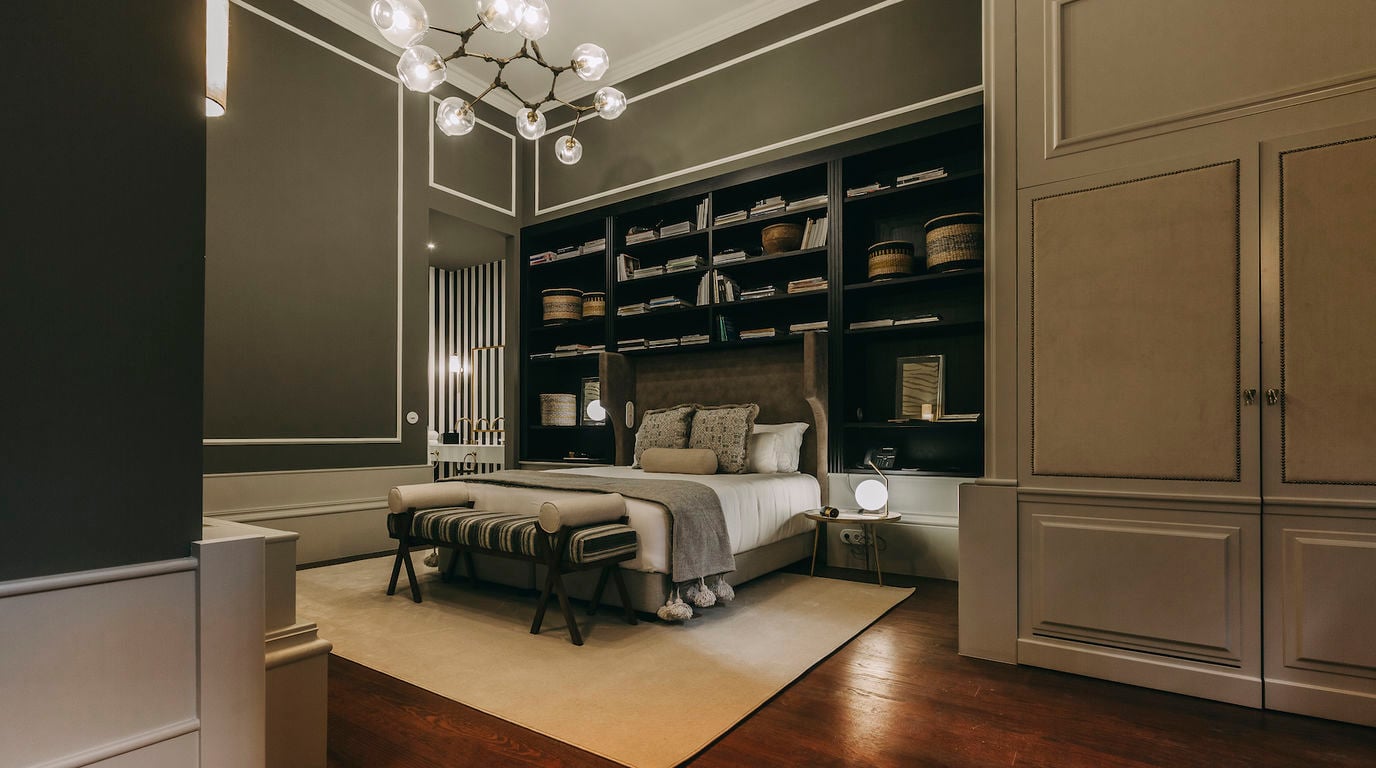 Torel 1884, Portugal — Contemporary luxury bedroom with dark built-in shelving, brass accents, geometric lighting fixture, and neutral palette blending modern design with classical architecture.