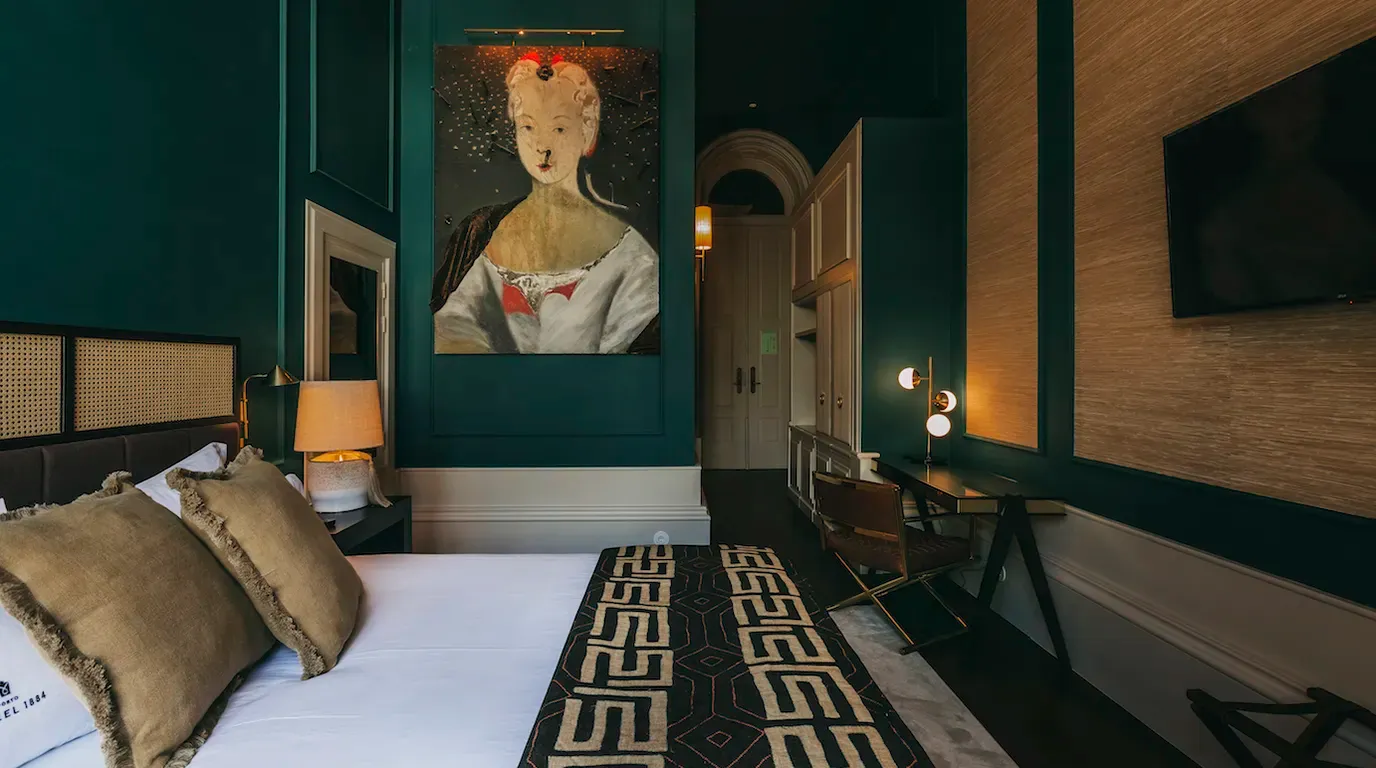 Torel 1884, Portugal — Teal bedroom with wood paneling, portrait artwork, geometric patterned runner, brass fixtures, and warm ambient lighting.