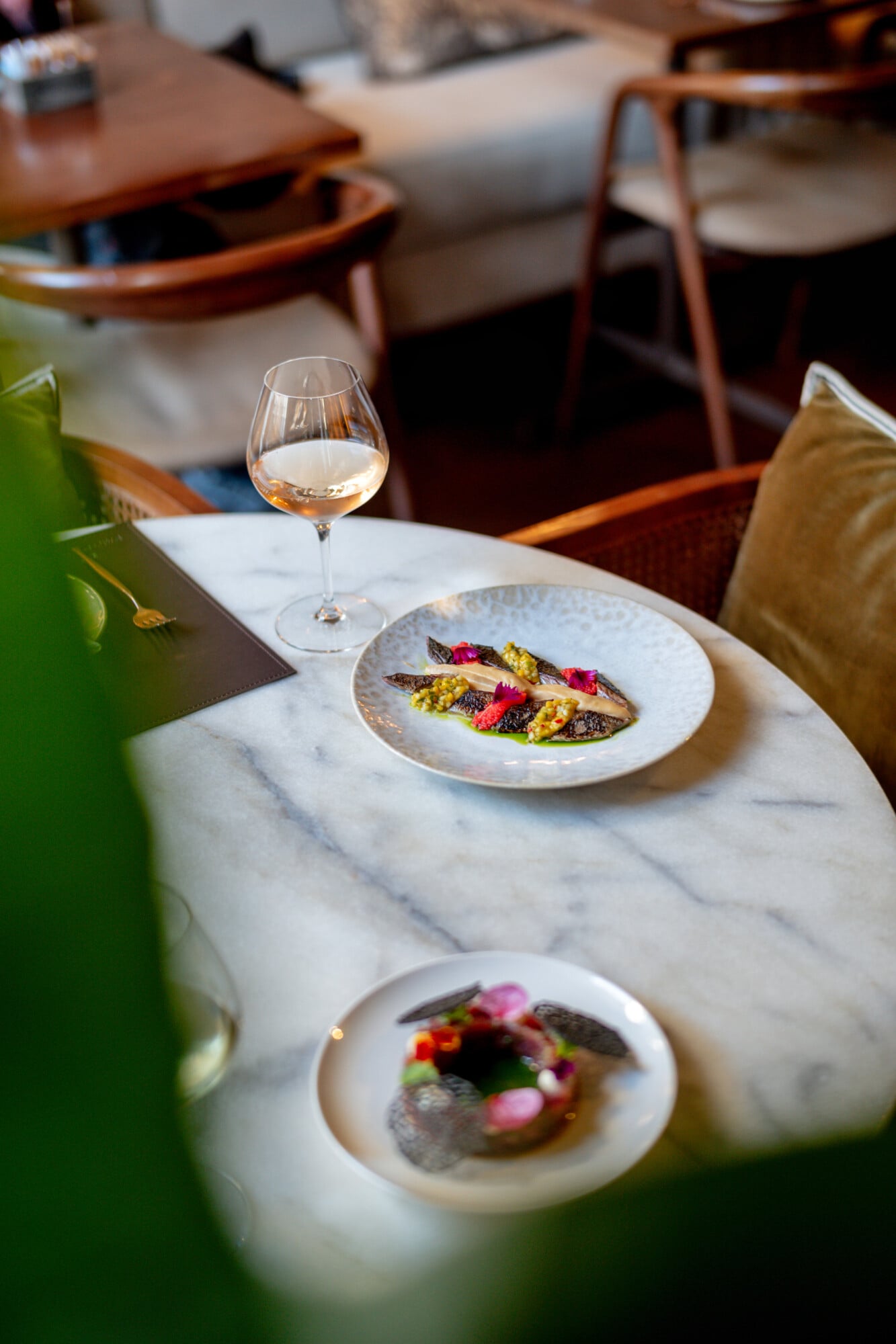 Torel 1884, Portugal — Marble dining table with plated fish and vegetable dishes, rosé wine glass, mid-century wooden chairs, warm natural light, fine dining interior.