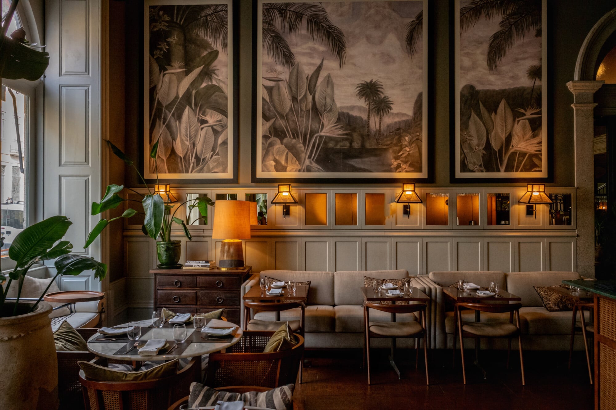 Bartolomeu Bistro & Wine, Portugal — Botanical framed artwork above banquette seating, warm ambient lighting, mid-century wood furnishings, and lush plants in intimate dining space.