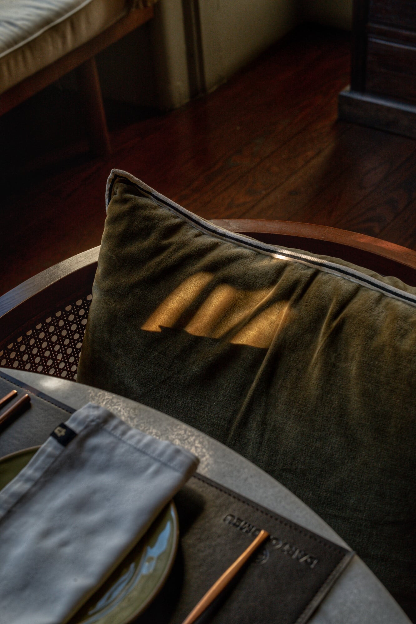 Torel 1884, Portugal — Olive linen pillow with sunlit pleats on wooden chair beside leather-bound books in warmly lit interior.