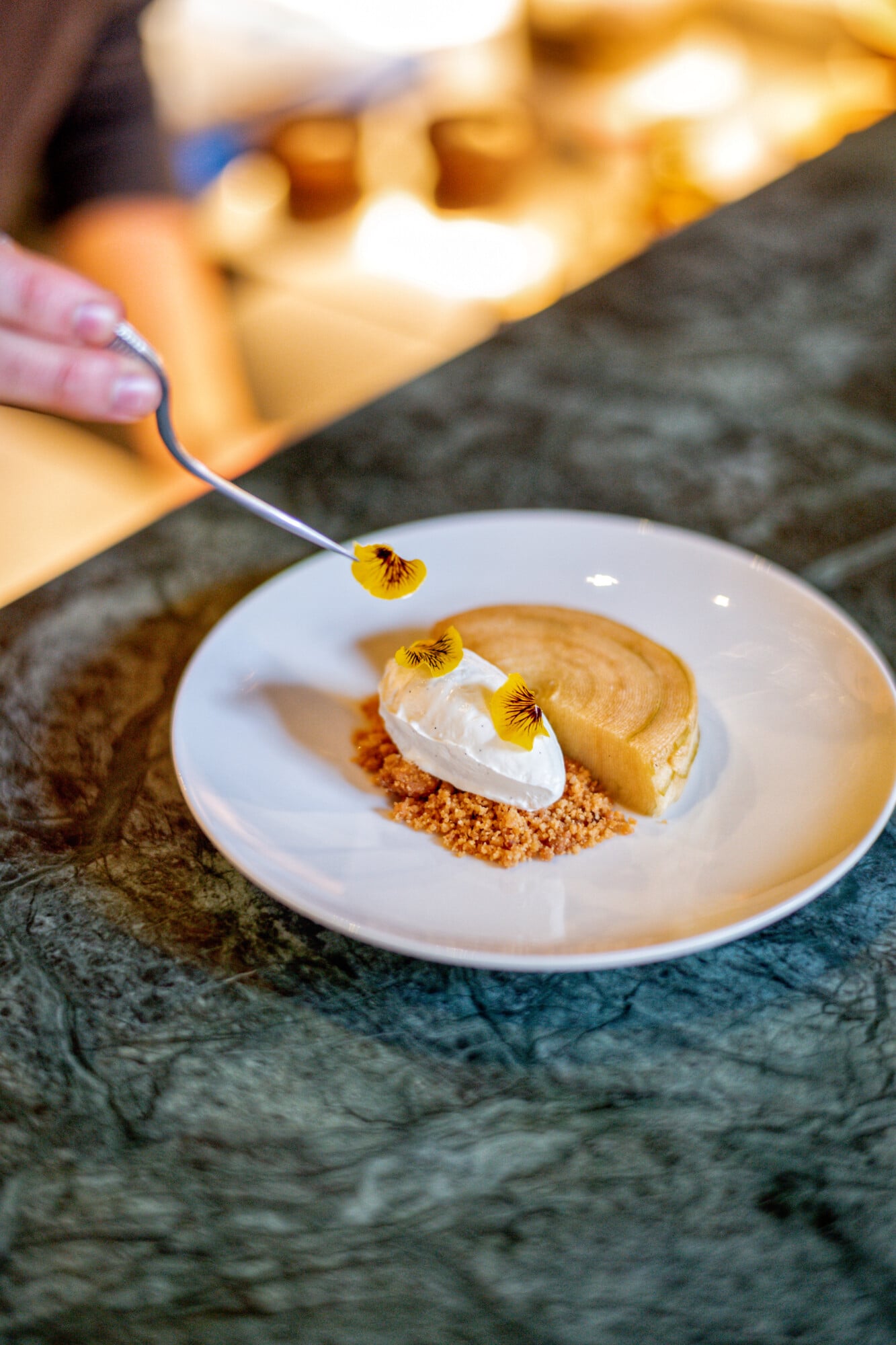 Torel 1884, Portugal — Plated dessert with peanut mousse, crisp crumble, whipped cream, and edible pansy flowers on slate surface, fine dining presentation.