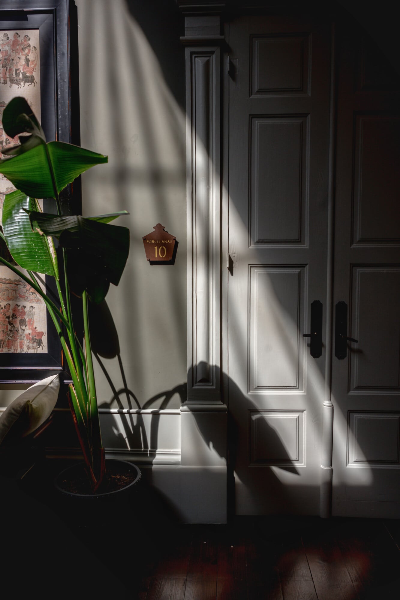 Torel 1884, Portugal — White paneled door with brass number 10, dappled sunlight and plant shadow, minimalist luxury entryway