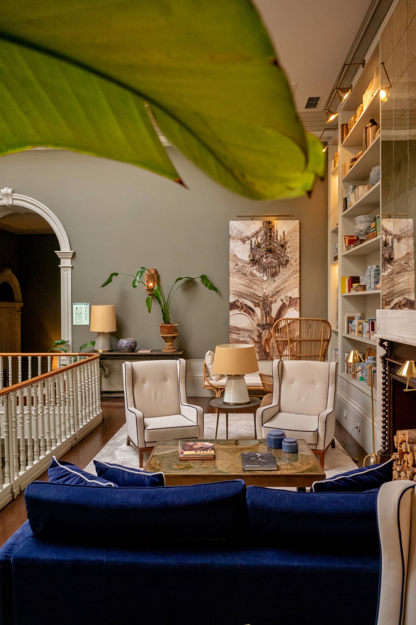 Torel 1884, Portugal — Elegant living room with navy velvet sofa, cream wingback chairs, wooden side table, brass accents, open shelving, and lush green plant against soft beige walls.