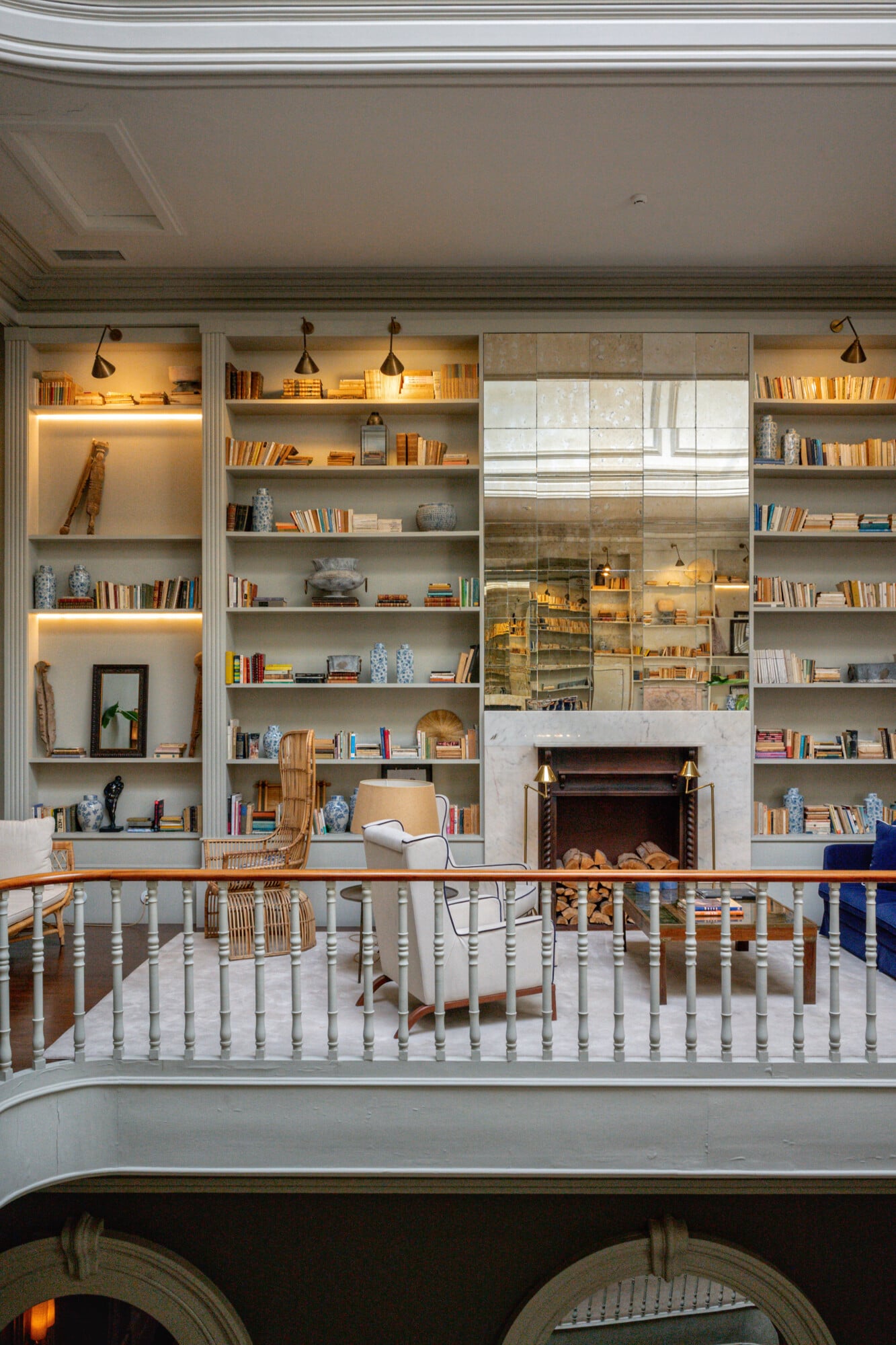 Torel 1884, Portugal — Floor-to-ceiling shelving with warm brass lighting, blue-and-white ceramics, leather chairs, and a marble fireplace in a luxury library lounge.
