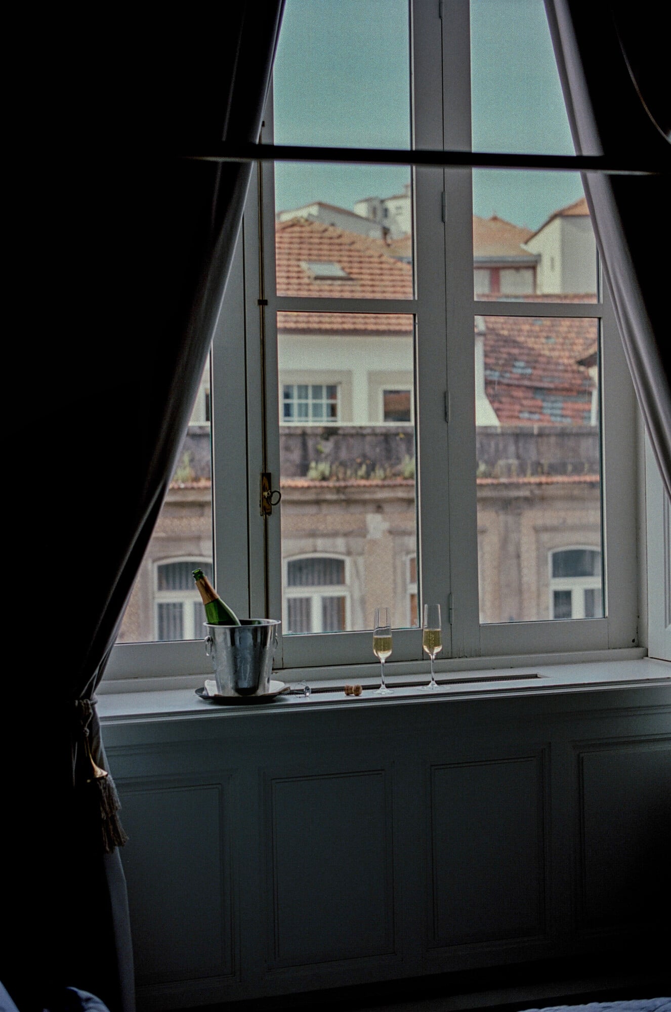 Torel 1884, Porto, Portugal — Champagne flutes and bottle in ice bucket on windowsill overlooking terracotta-roofed European architecture under clear sky.