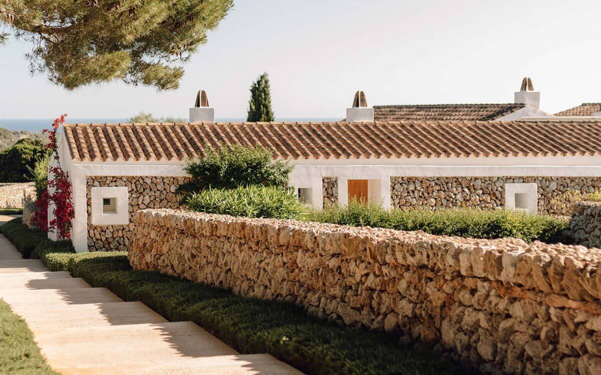 Torralbenc, Balearic Islands — Mediterranean stone villa with terracotta tile roof, white-rendered walls, manicured hedges, and sea views beyond, showcasing rural luxury architecture.