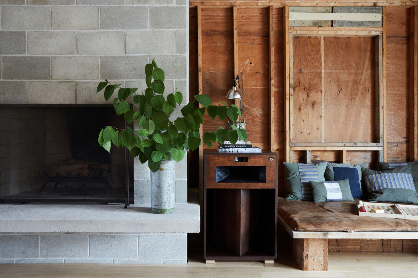 Tourists, North America — Minimalist hotel interior with concrete fireplace, wooden built-ins, potted plant, and striped upholstered seating in muted tones.