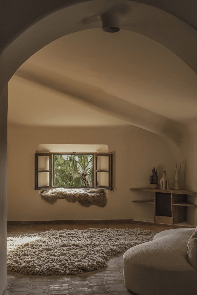 Hotel Corazón, Balearic Islands, Spain — Arched stone room with palm-view window, natural textiles, minimalist wooden shelving, warm Mediterranean light.