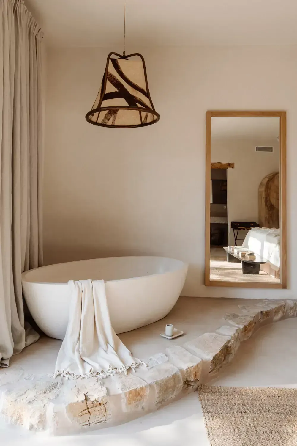 Finca La Inika, Balearic Islands — Minimalist bathroom with sculptural white stone bathtub, woven pendant light, floor-to-ceiling mirror, and natural limestone accents.