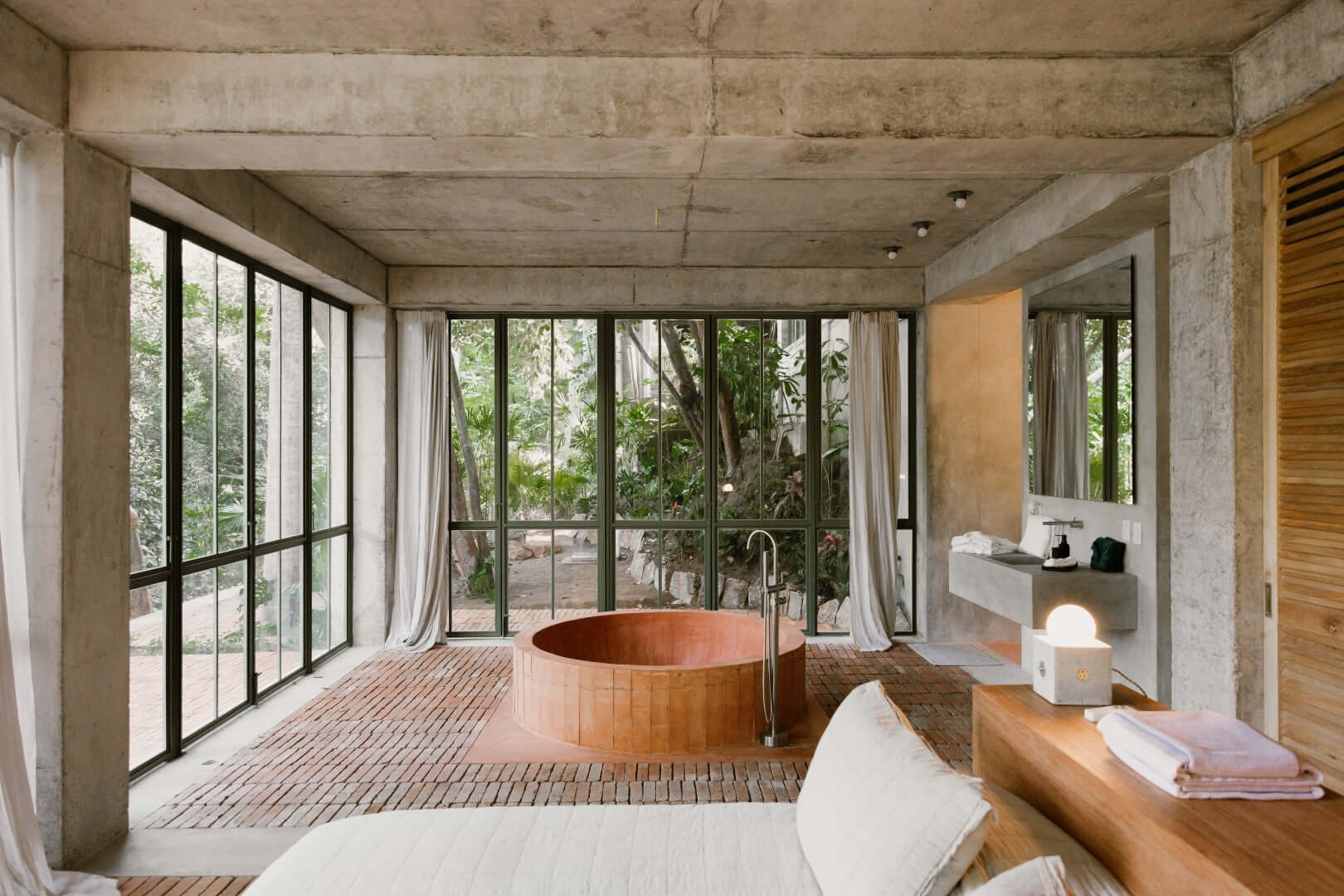 NICO, Mexico — Concrete bathroom with wooden soaking tub, floor-to-ceiling windows overlooking lush garden, minimalist design, natural light.